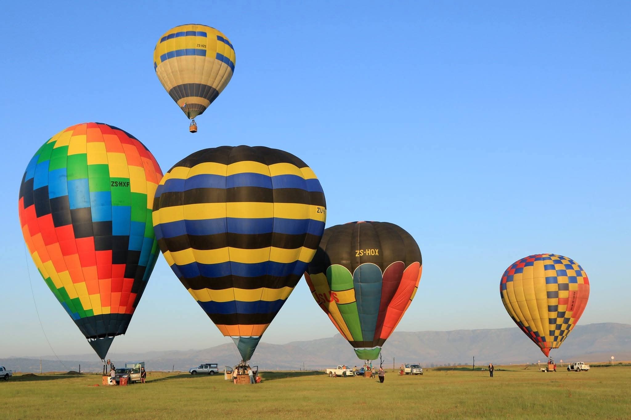 Hot-air balloons inflating on an open field at sunrise, mountains behind