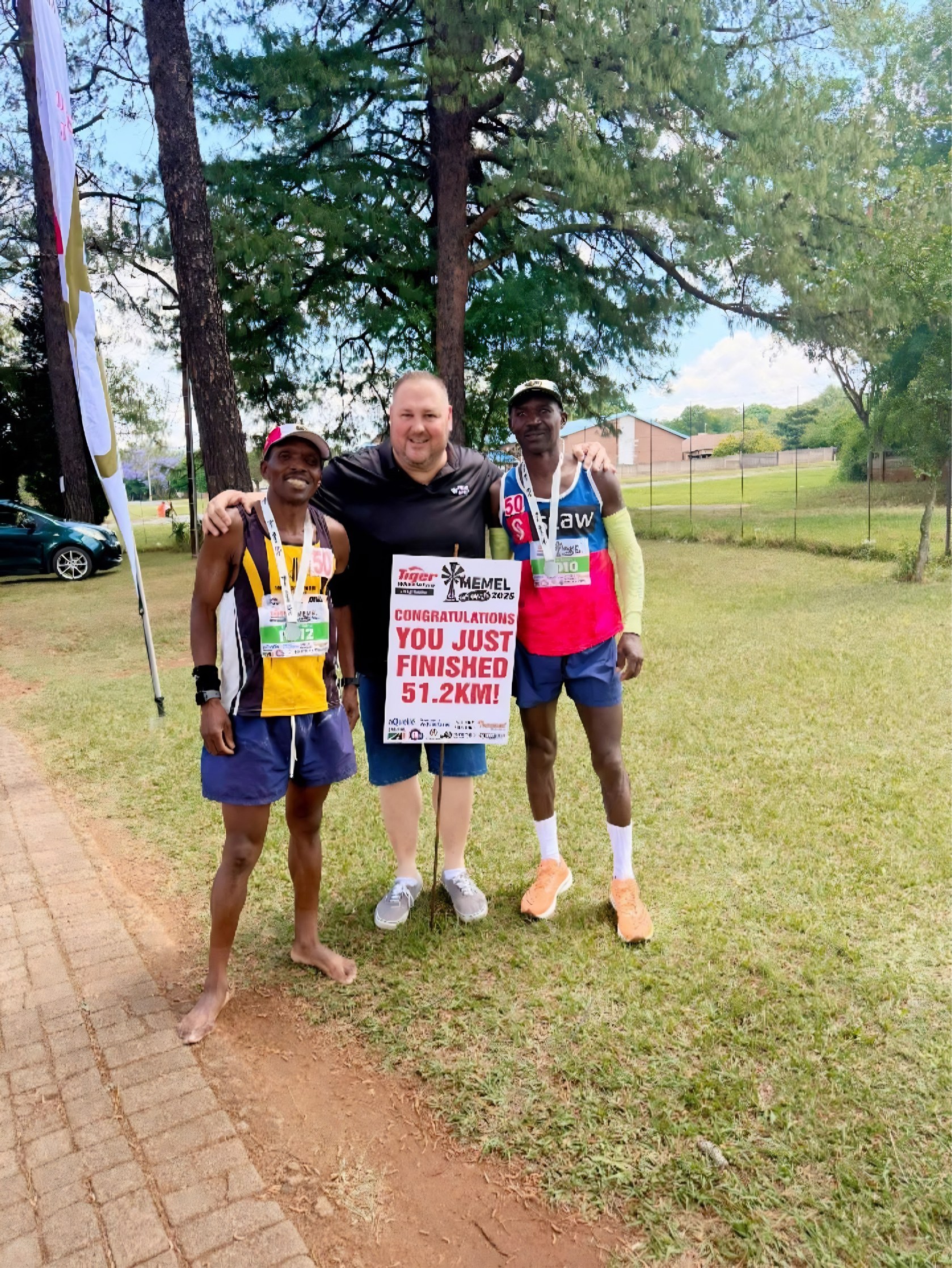 Two finishers with Johan Pieters and a sign reading: Congratulations, you just finished 51.2 km