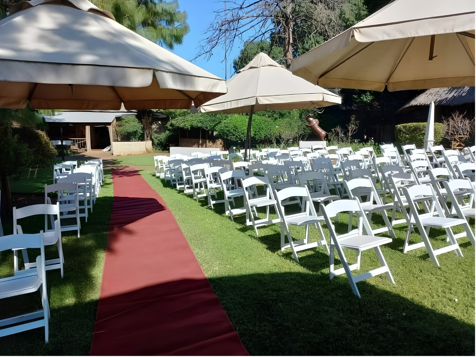 White chairs on the lawn either side of a red carpet aisle, under umbrellas in the garden at The Pines