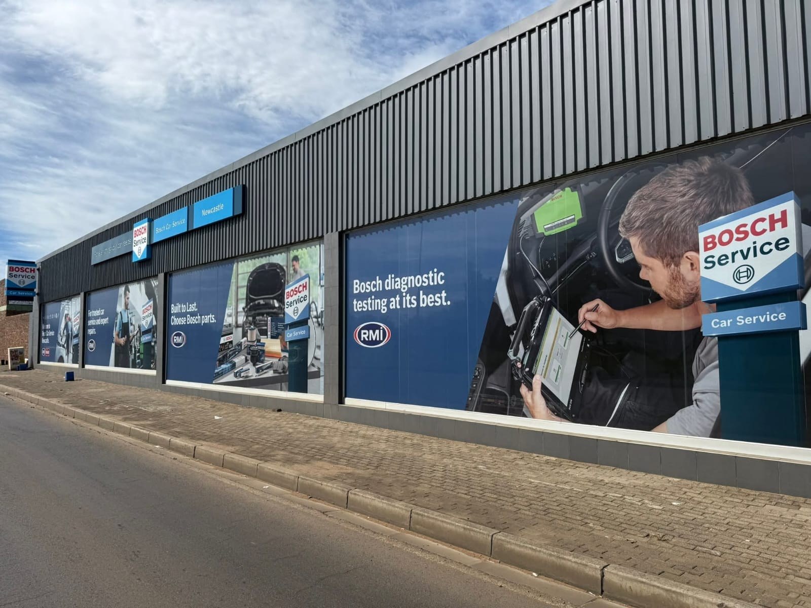 Large window graphics along the Bosch Car Service building in Newcastle, a technician with a diagnostic tablet on the nearest window